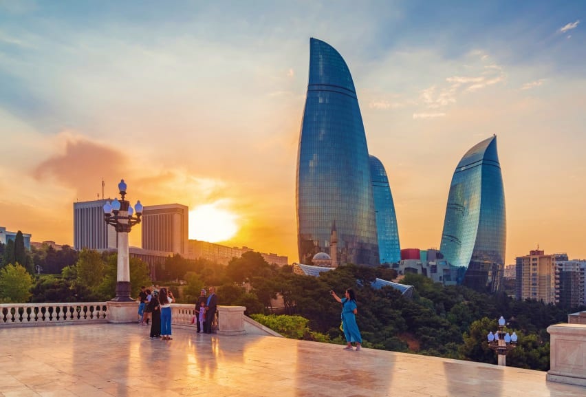 Flame Towers at sunset in Baku, Azerbaijan, viewed from a terrace with tourists and historic architecture in foreground